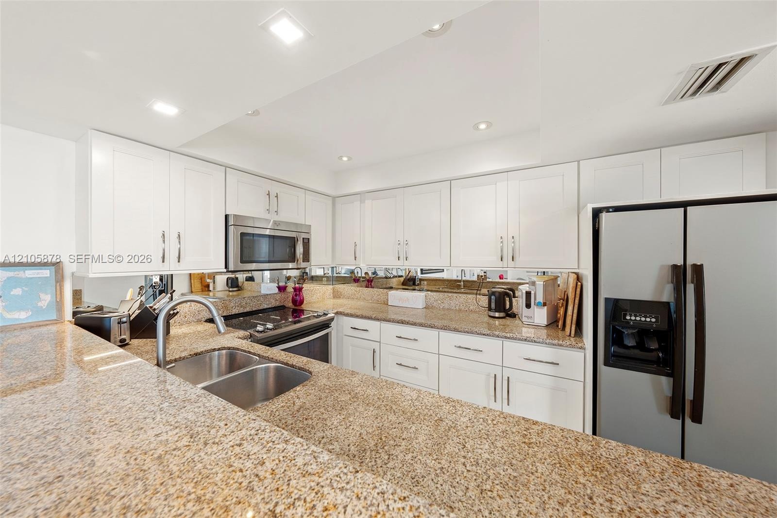 Kitchen featuring white shaker-style cabinetry, expansive stone countertops, stainless steel appliances, a double-basin undermount sink, and mirrored 