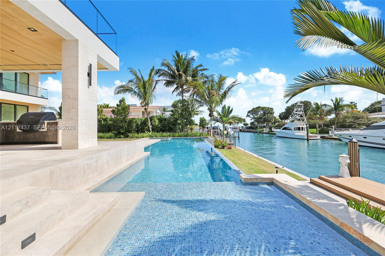 Waterfront lap pool featuring tiled finishes, stone decking, and a built-in outdoor kitchen