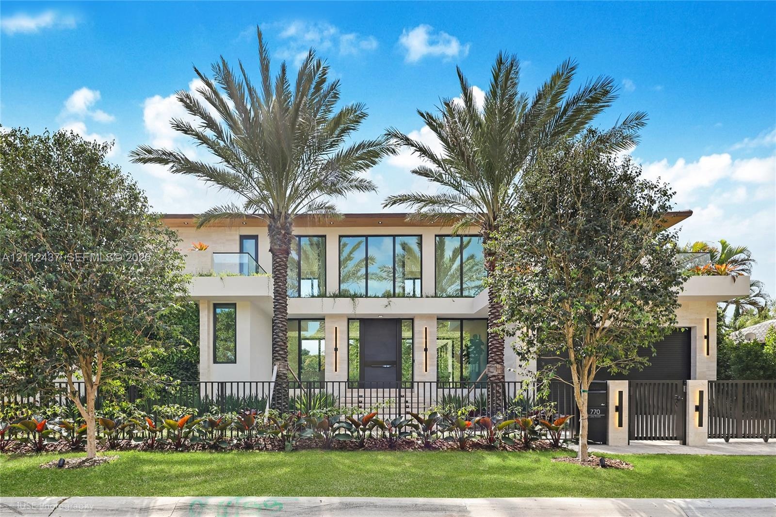 Contemporary two-story exterior featuring smooth stucco facade, floor-to-ceiling glass windows, integrated wall-mounted lighting, manicured landscapin