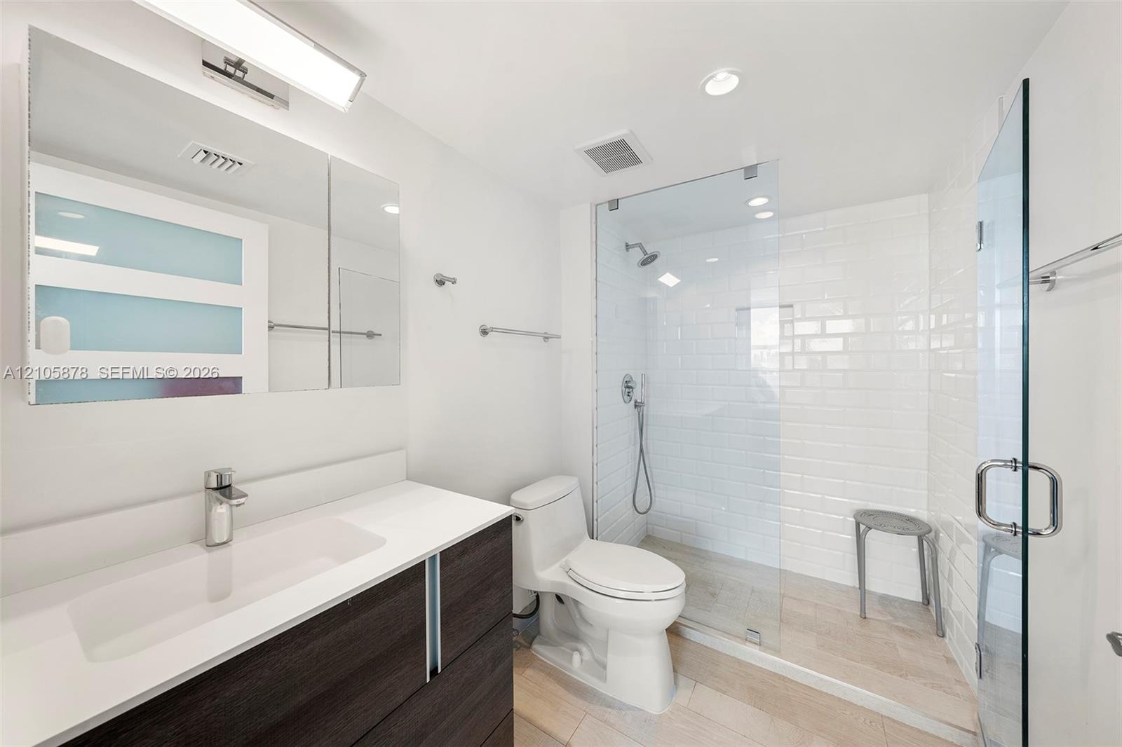Dark-finish floating vanity with a white countertop and rectangular integrated sink, walk-in shower with white subway tile surround and glass enclosur