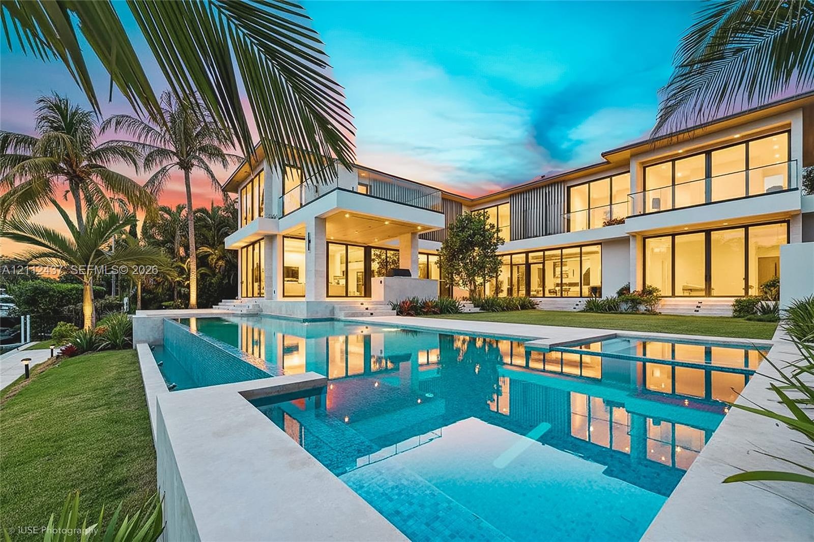 Two-story contemporary residence featuring expansive floor-to-ceiling glass walls, an infinity-edge pool, multiple covered balconies with glass railin