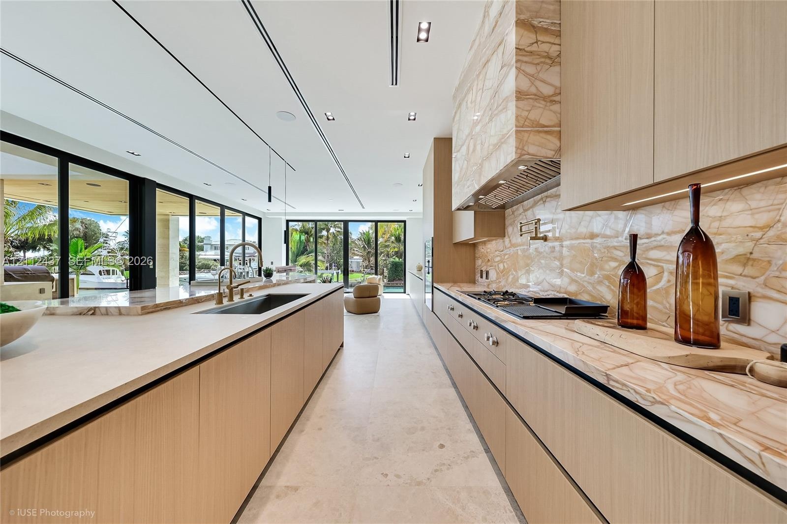 Custom wood-finish cabinetry, expansive stone-topped kitchen island with waterfall edge, integrated stainless steel appliances, and floor-to-ceiling g