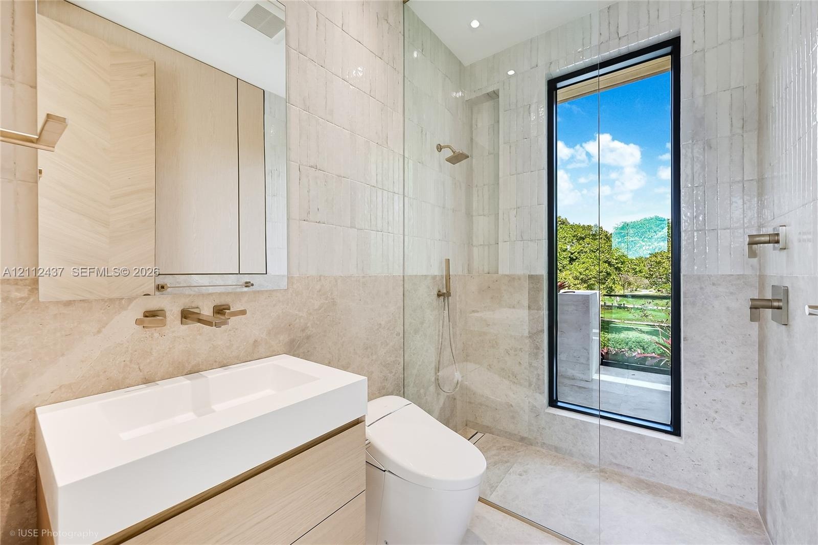 Modern bathroom featuring a wood-finish floating vanity, wall-mounted metallic fixtures, a frameless glass shower enclosure, large-format stone tiling