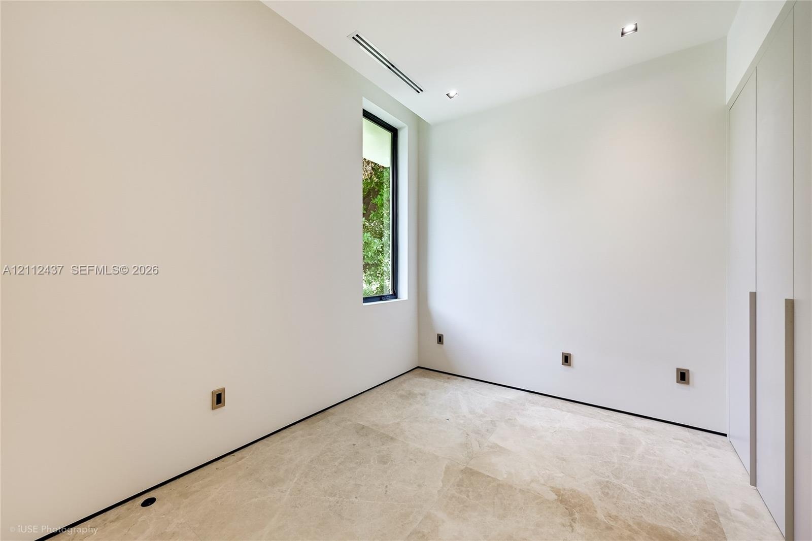 Minimalist room featuring natural stone flooring, floor-to-ceiling built-in cabinetry, recessed lighting, and a vertical window