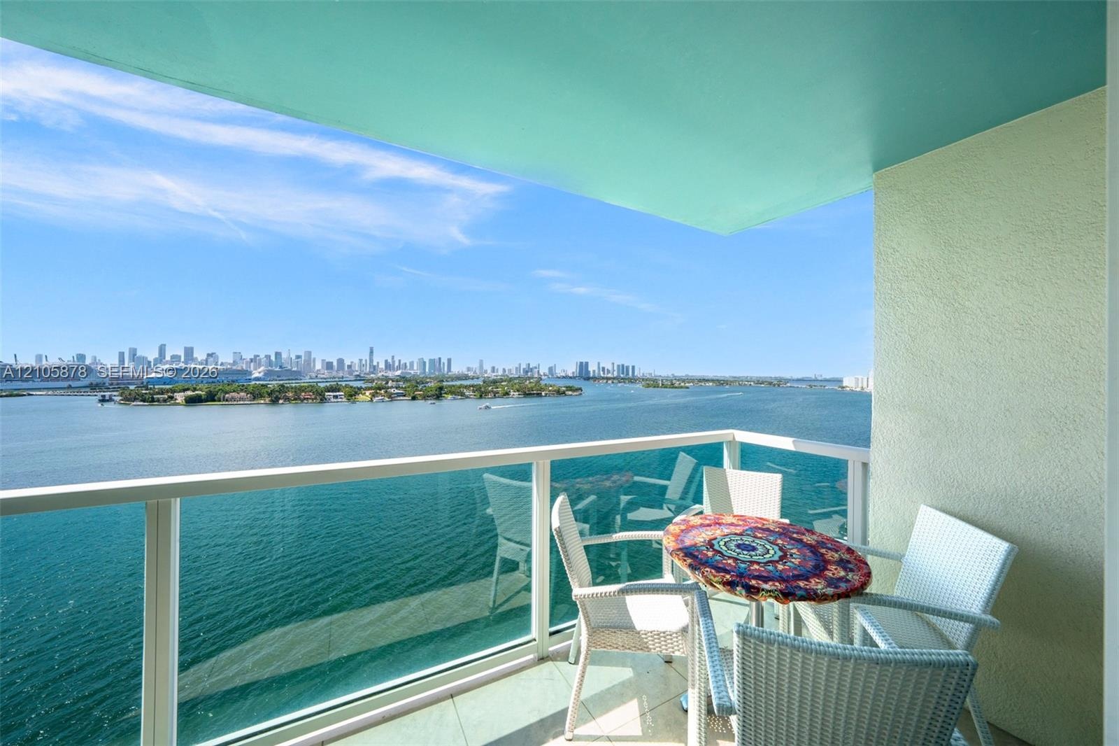 Covered balcony featuring glass railing, tiled flooring, and cityscape scenery across the water