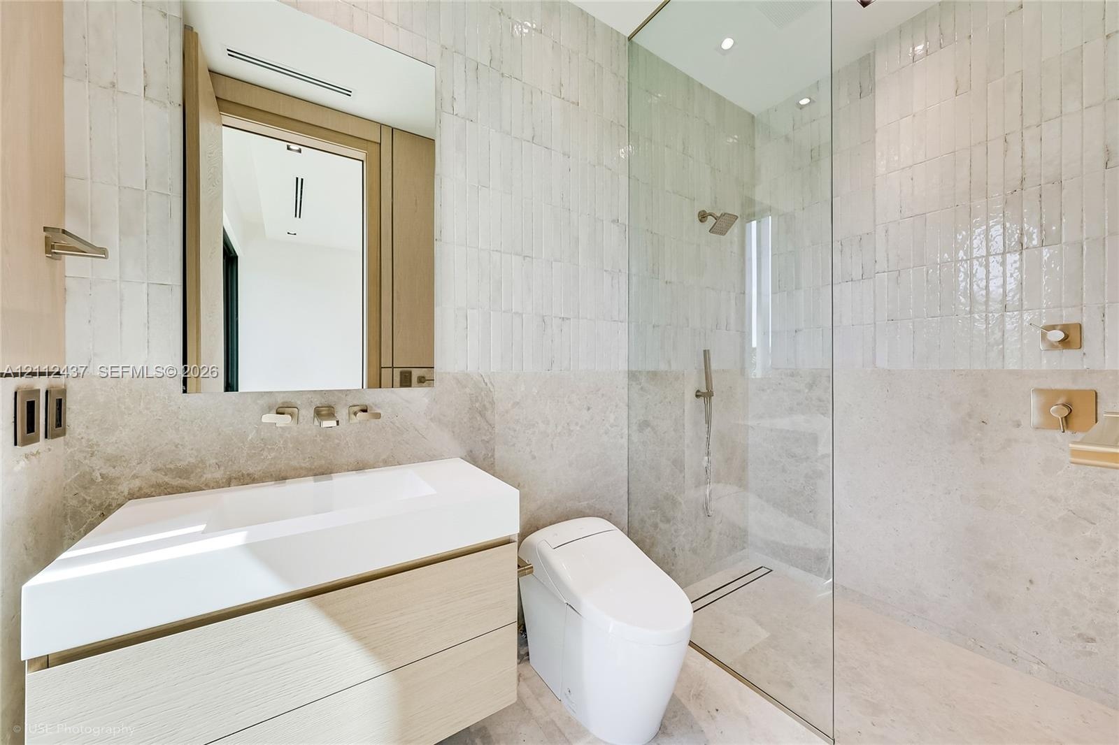 Floating vanity with integrated sink, glass-enclosed walk-in shower, wall-mounted brushed metal plumbing fixtures, and textured stone wall tile