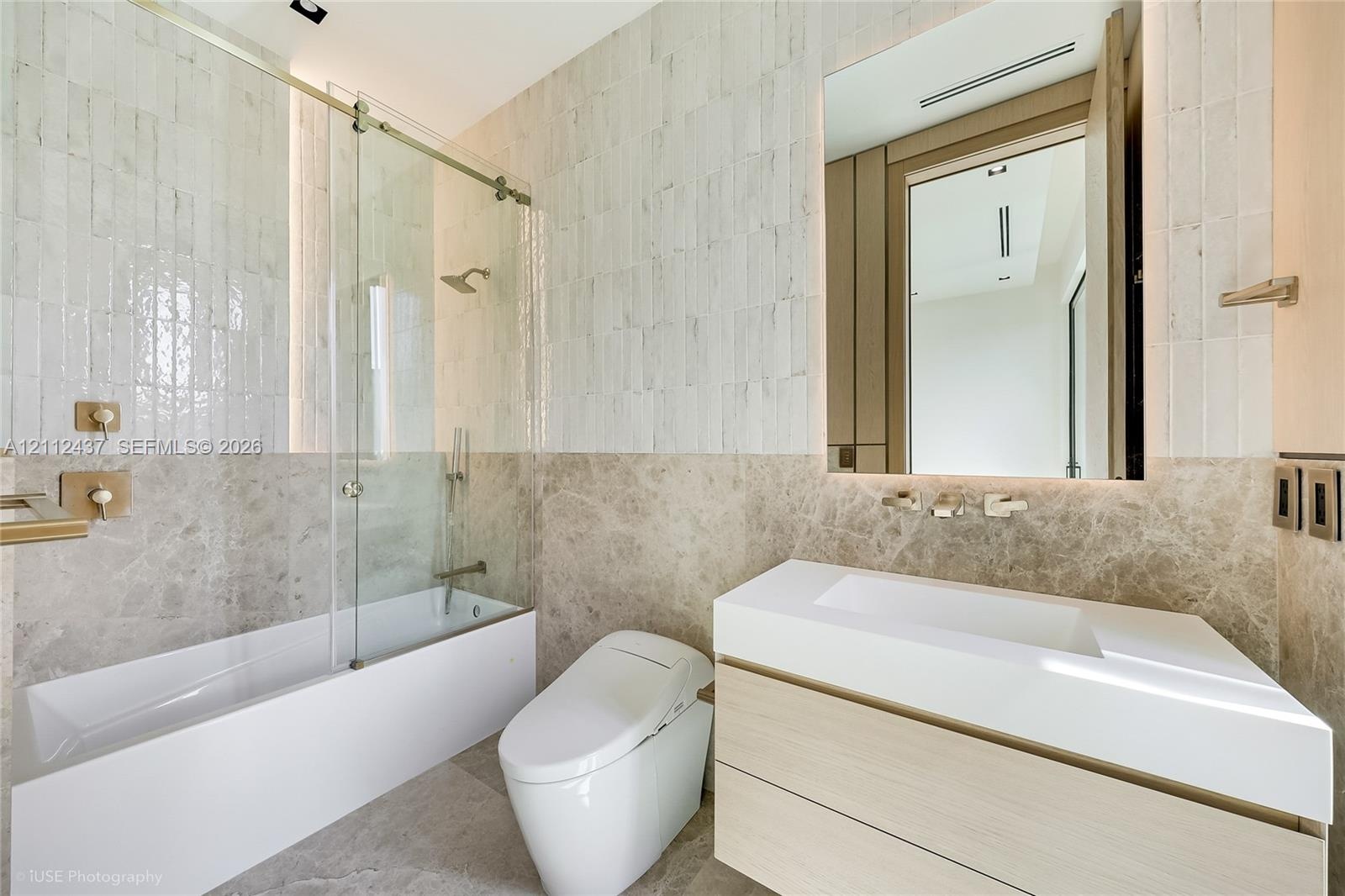 Bathroom featuring a floating vanity with a white countertop, wall-mounted faucet, glass-enclosed soaking tub with stone tile surround, and textured w