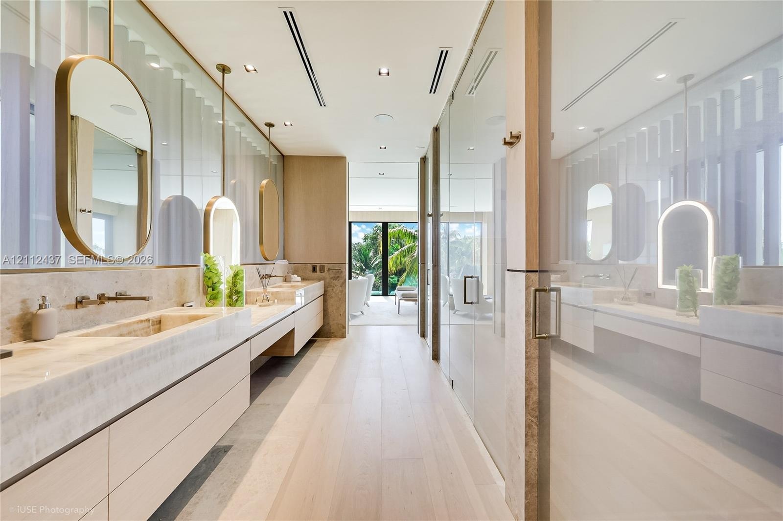 Dual floating vanities with integrated stone sinks and wall-mounted faucets, suspended oval mirrors, recessed ceiling lighting, wood-finish flooring, 