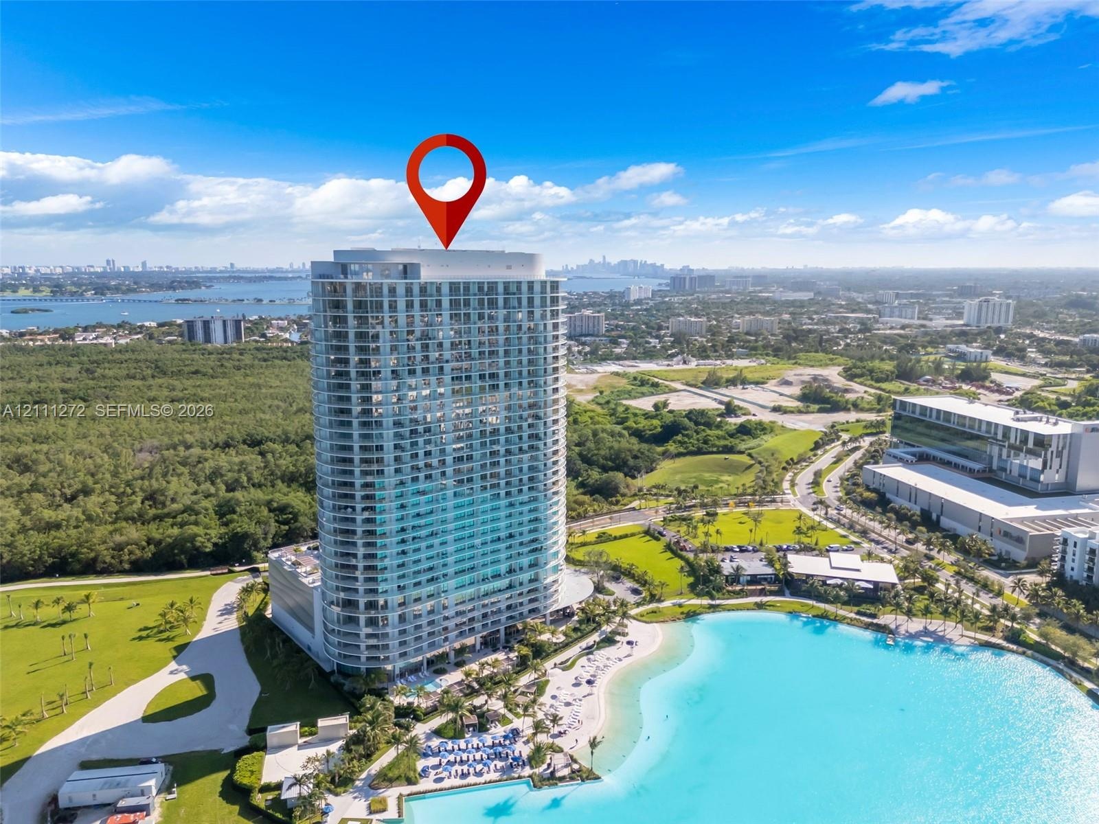 High-rise residential tower featuring a glass facade, private balconies, and proximity to an expansive man-made lagoon with a sandy beach