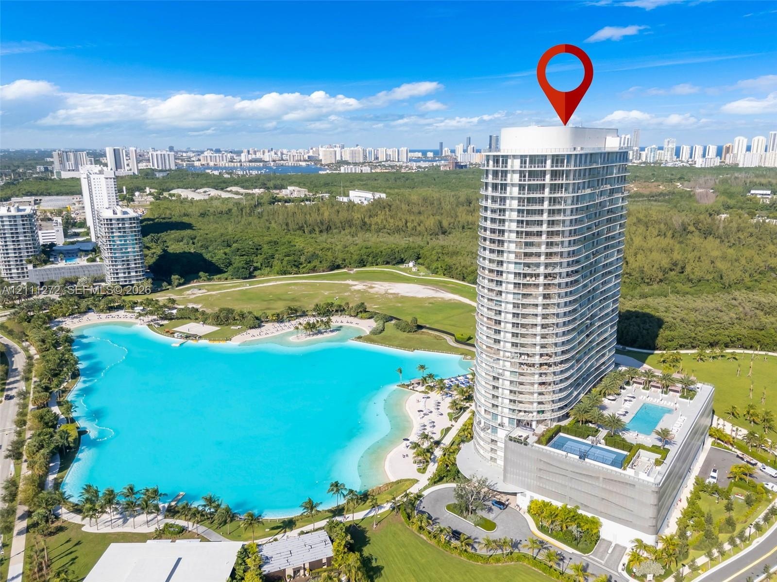 High-rise residential tower featuring extensive balcony access, a multi-level podium structure, ground-level swimming pools, and an expansive man-made