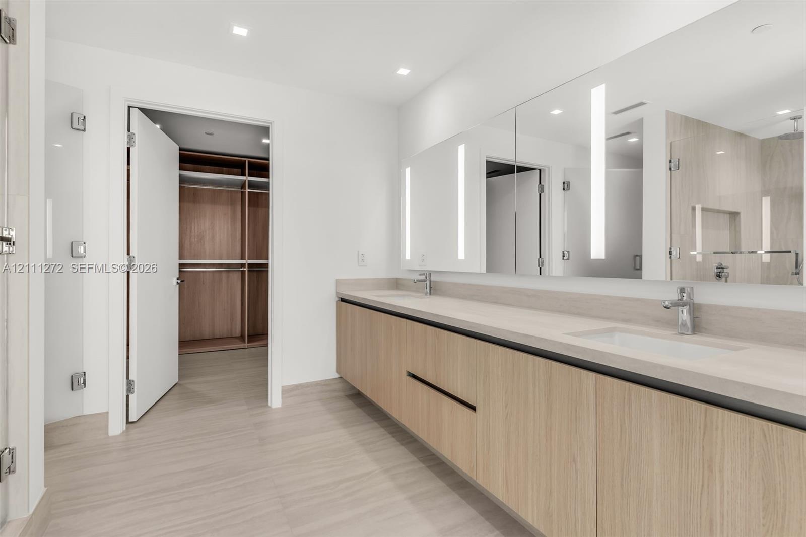 Floating vanity with dual rectangular undermount sinks, sleek wood-finish cabinetry, expansive wall-to-wall mirror with integrated lighting, and a wal
