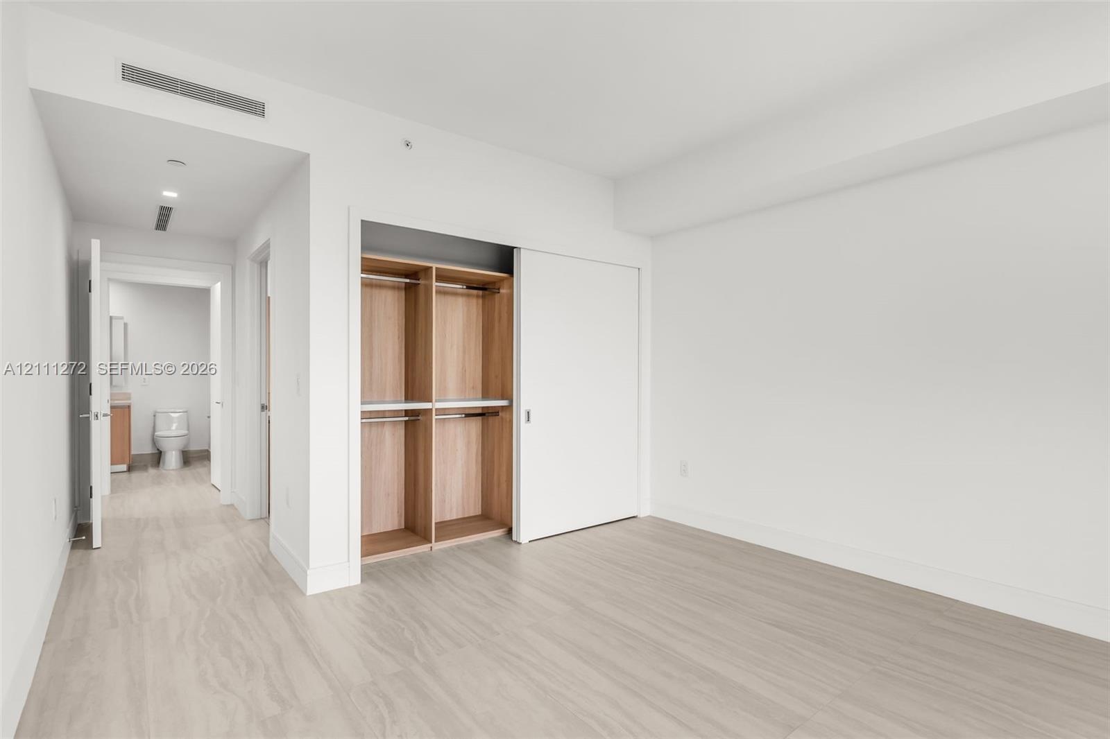 Wood-finish flooring, sliding door closet with built-in wooden shelving, and recessed ceiling lighting