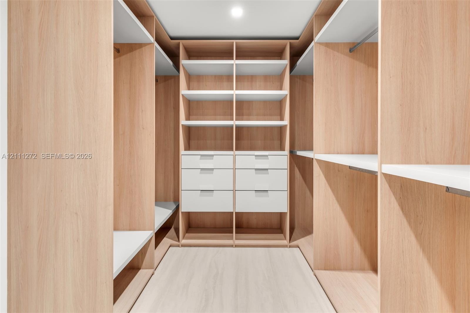 Custom walk-in closet featuring floor-to-ceiling wood-finish cabinetry, built-in shelving, integrated hanging rods, and stacked drawer storage with cl