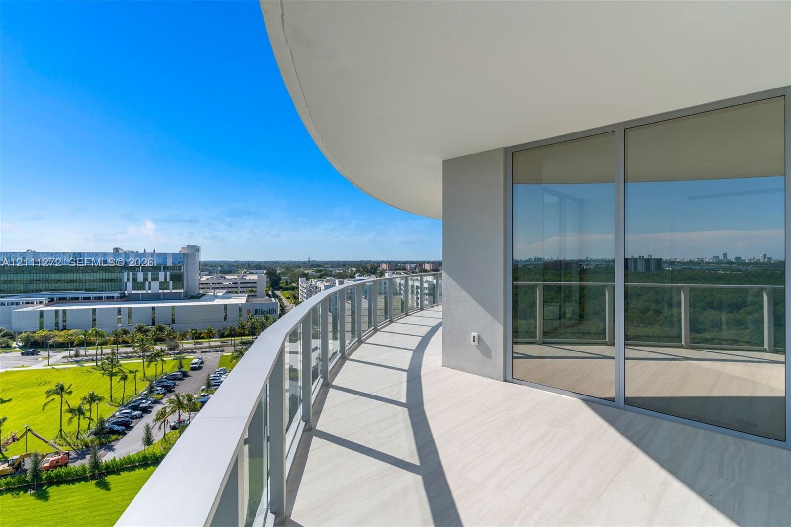 Curved balcony featuring light-toned tile flooring, glass panel railings, and floor-to-ceiling glass sliding doors