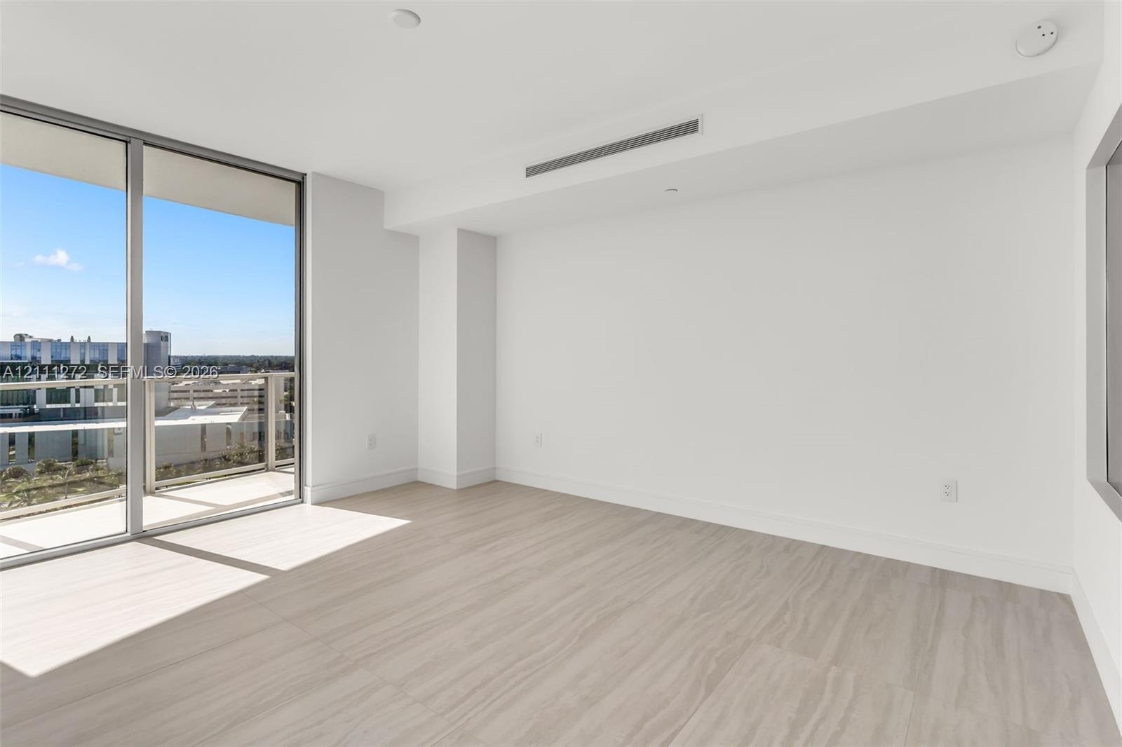 Floor-to-ceiling glass sliding doors, wood-finish flooring, private balcony with metal railing, and neutral wall palette