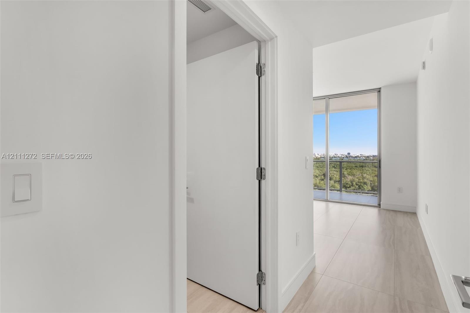 Floor-to-ceiling glass sliding doors, private balcony, neutral large-format tile flooring, and solid-core interior doors