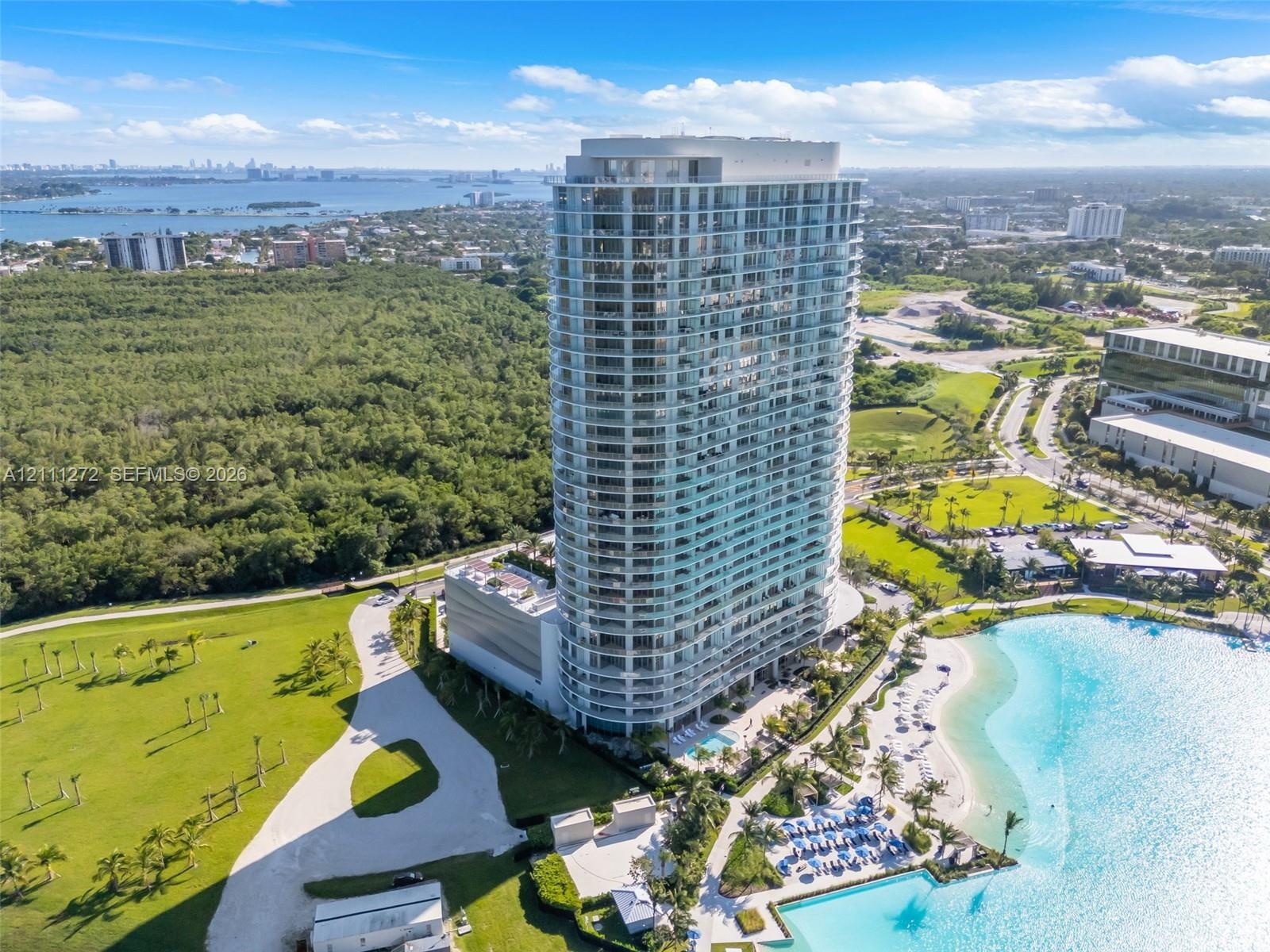 High-rise glass facade residential tower featuring wrap-around balconies, a ground-level swimming pool, and direct waterfront access