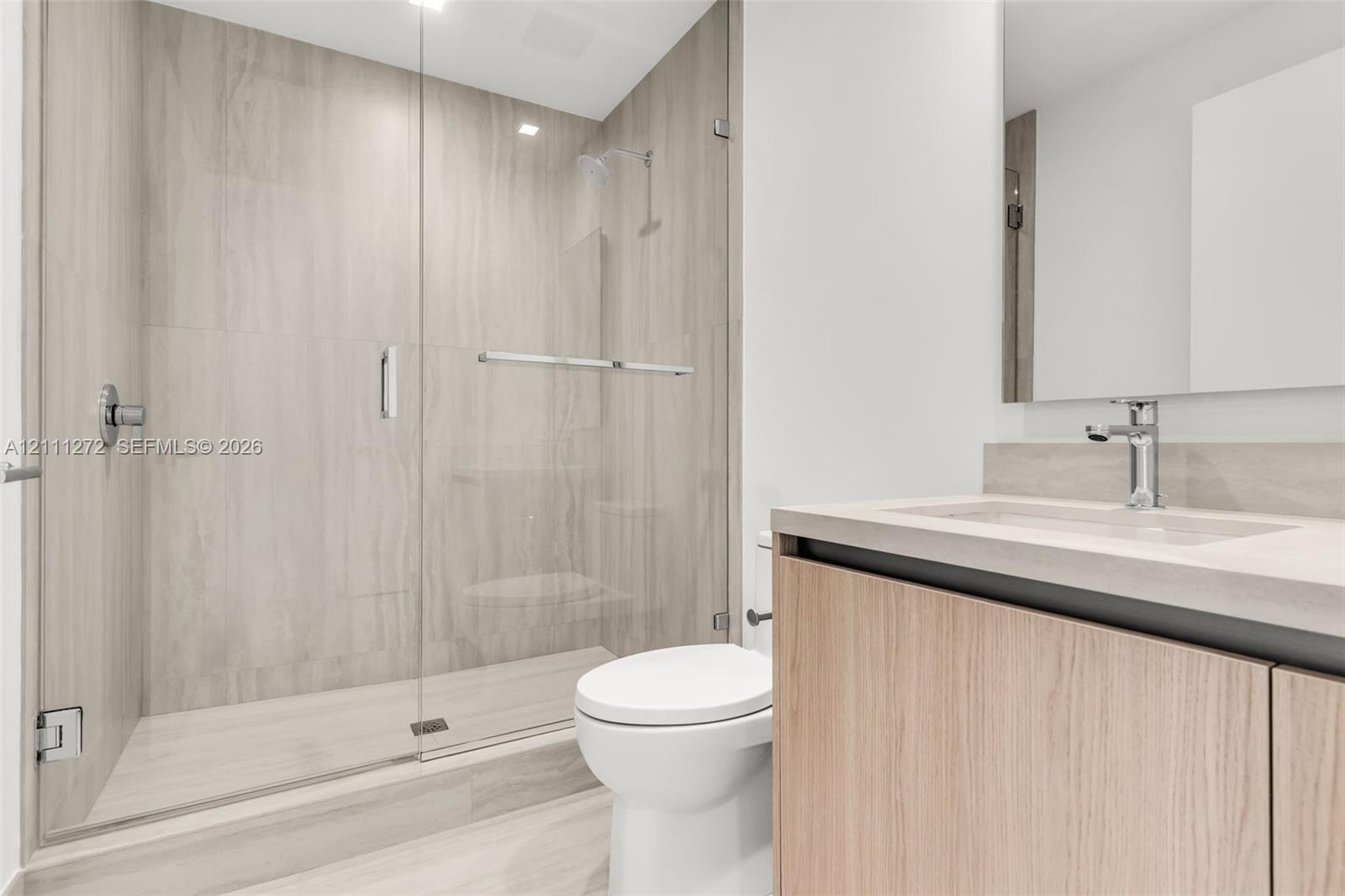 Walk-in glass-enclosed shower with large-format stone-finish tile surround, wood-finish floating vanity, integrated rectangular basin, and wall-to-wal