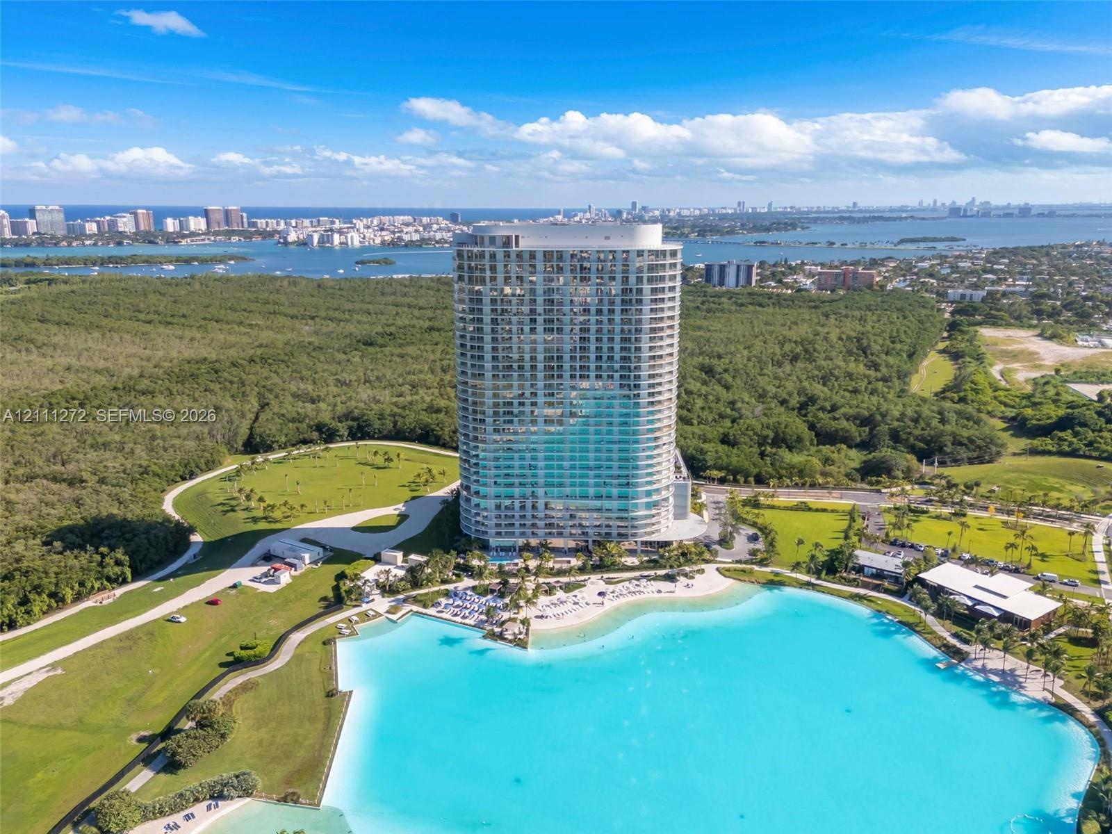 High-rise residential tower featuring a glass facade, expansive waterfront, landscaped grounds, and coastal surroundings