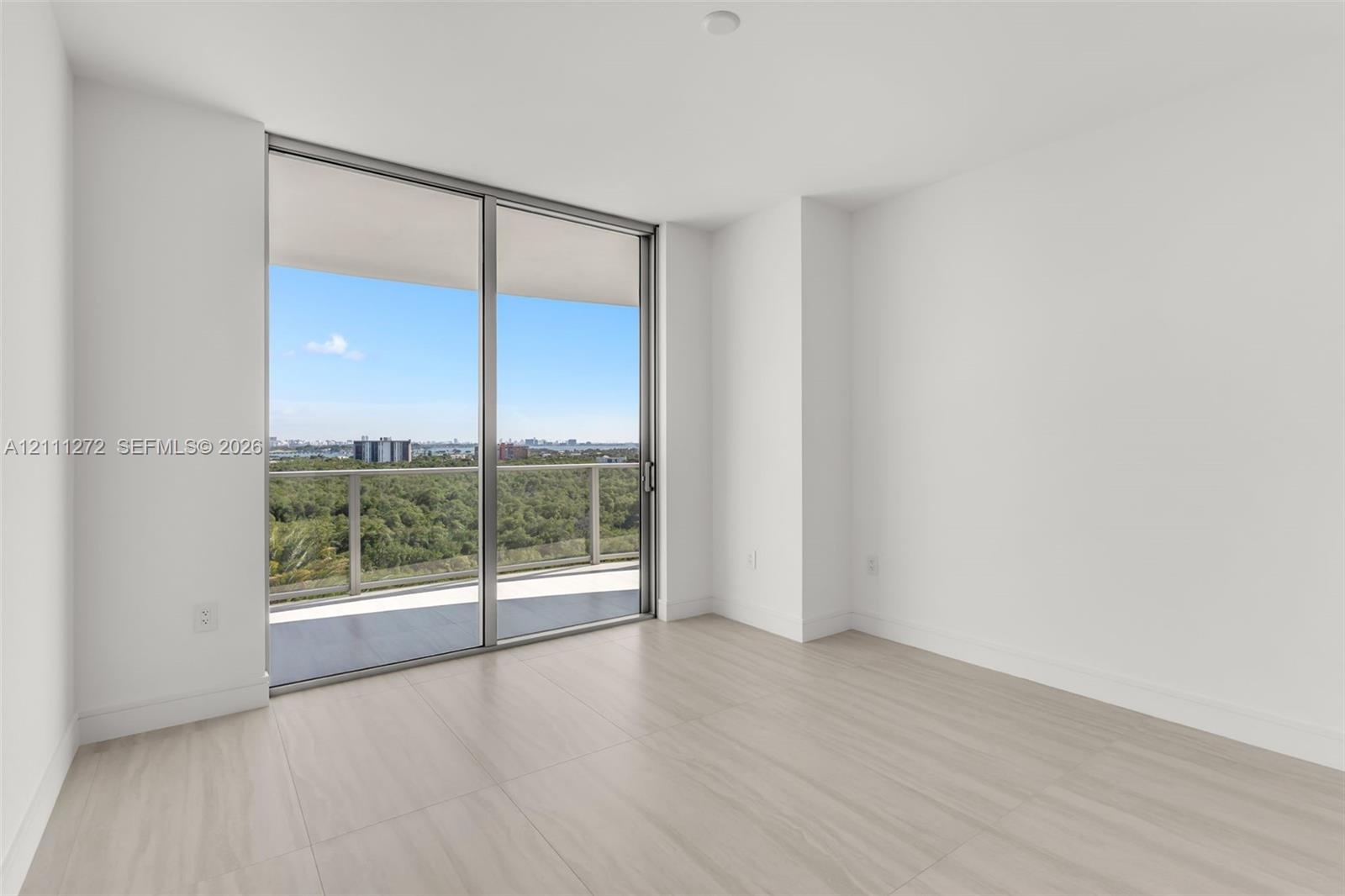Floor-to-ceiling sliding glass door, light-toned wood-finish flooring, and covered balcony with metal railing