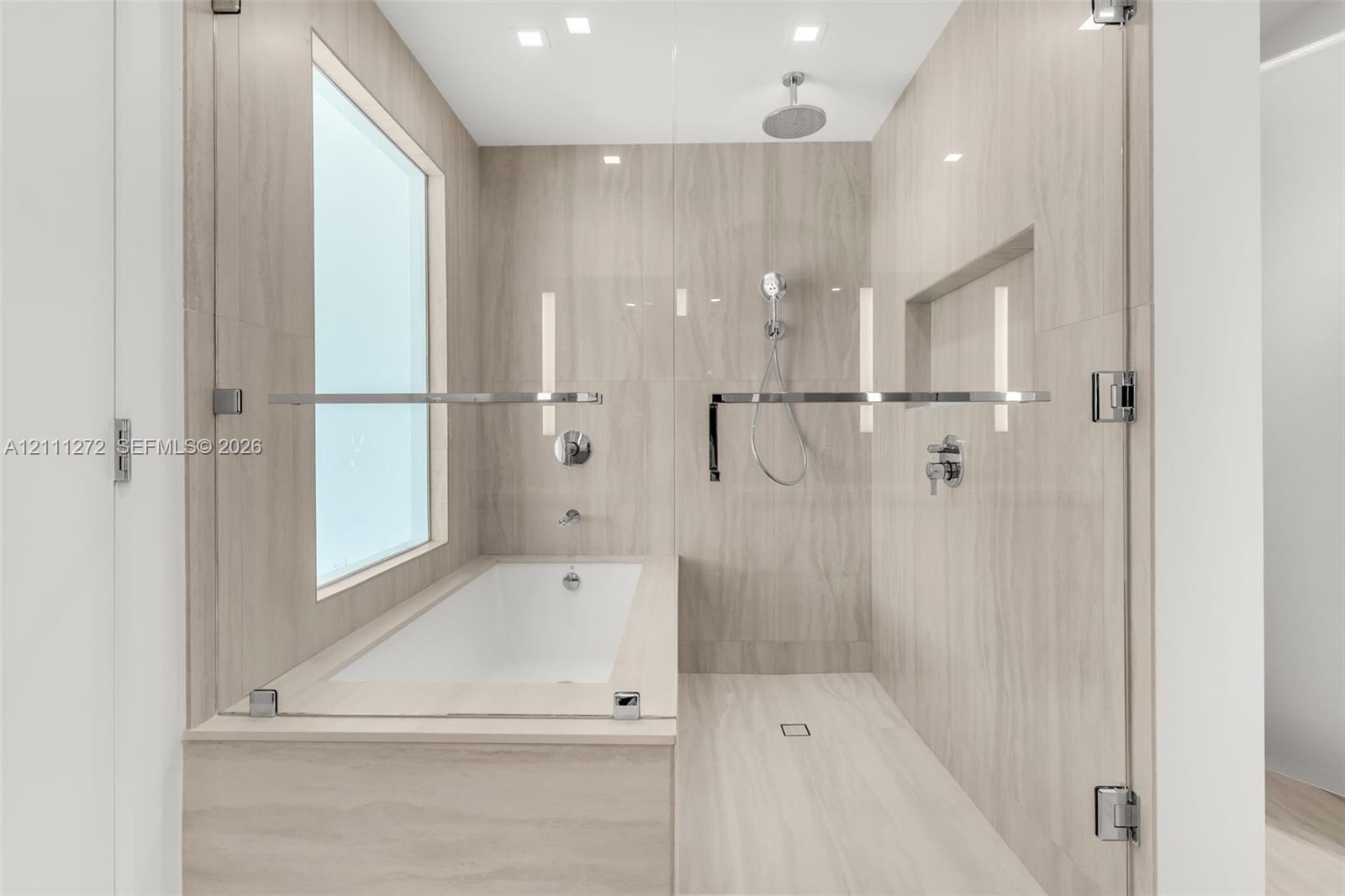 Wet room featuring large-format tile surround, integrated soaking tub, overhead rainfall showerhead, handheld sprayer, and recessed wall niche