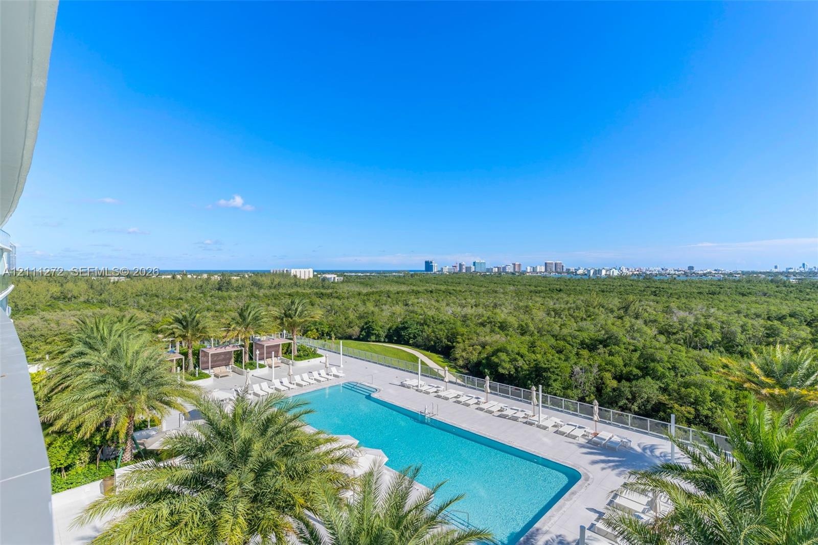 Swimming pool featuring a paved deck, perimeter fencing, palm tree landscaping, and coastal cityscape backdrop