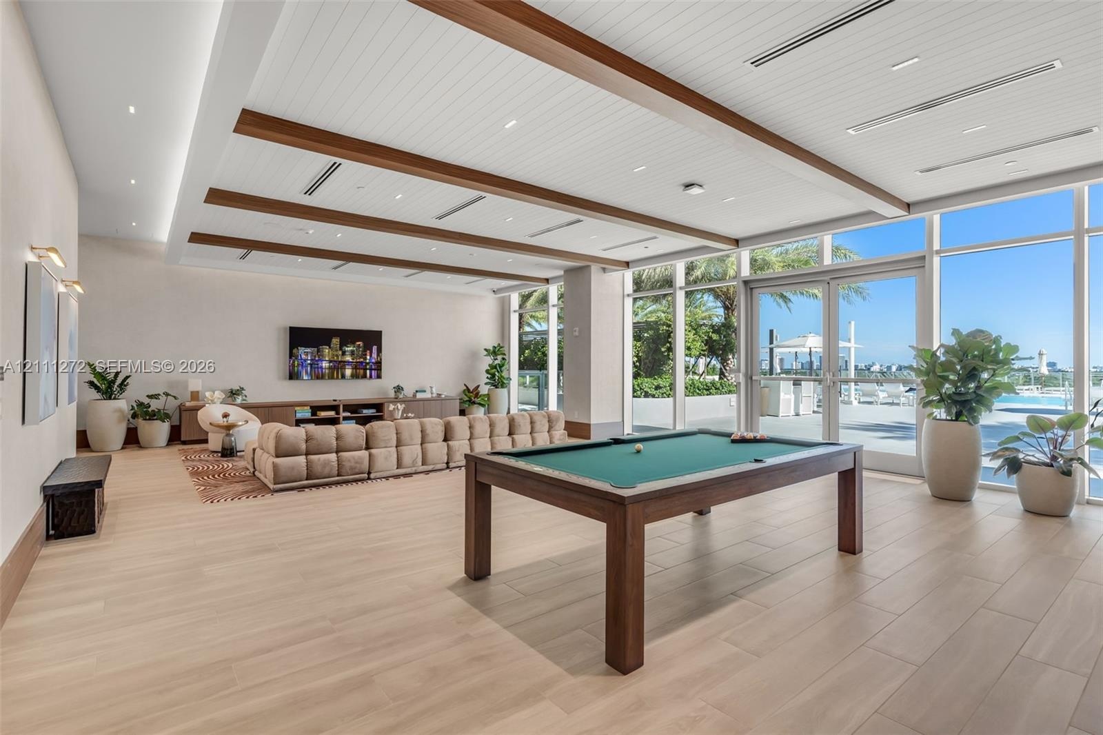 Spacious recreation area featuring a coffered ceiling with exposed wood beams, recessed lighting, expansive glass walls, and wood-finish flooring