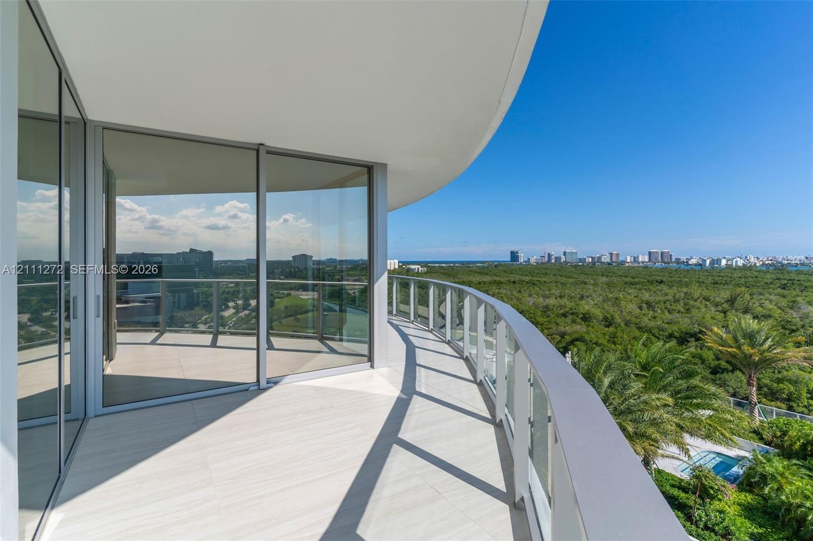 Curved wrap-around balcony featuring large-format tile flooring, floor-to-ceiling glass sliding doors, and a transparent glass railing