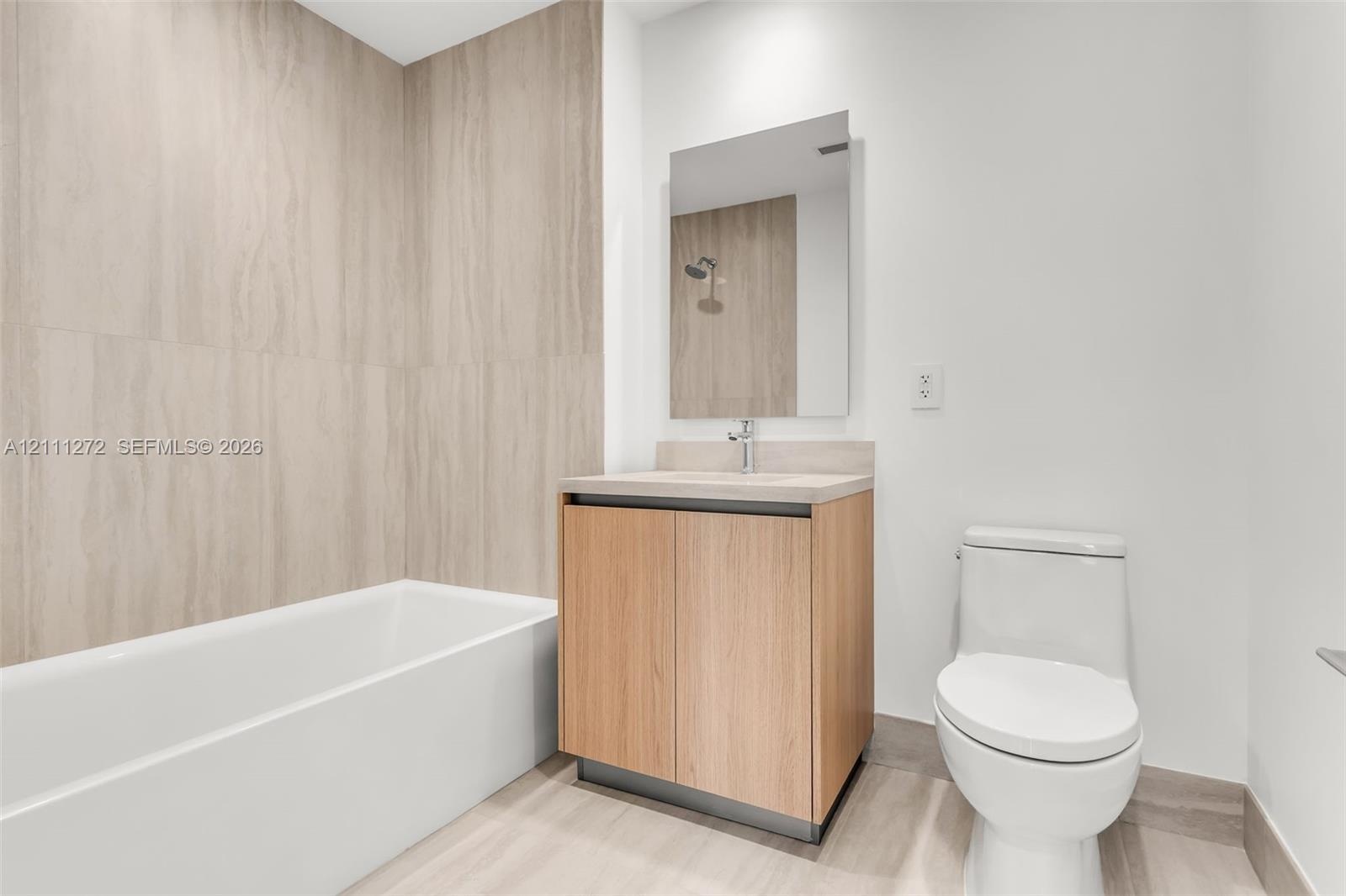 Bathroom featuring floor-to-ceiling textured tile surround, built-in vanity with wood-finish cabinetry, countertop basin, rectangular wall-mounted mir