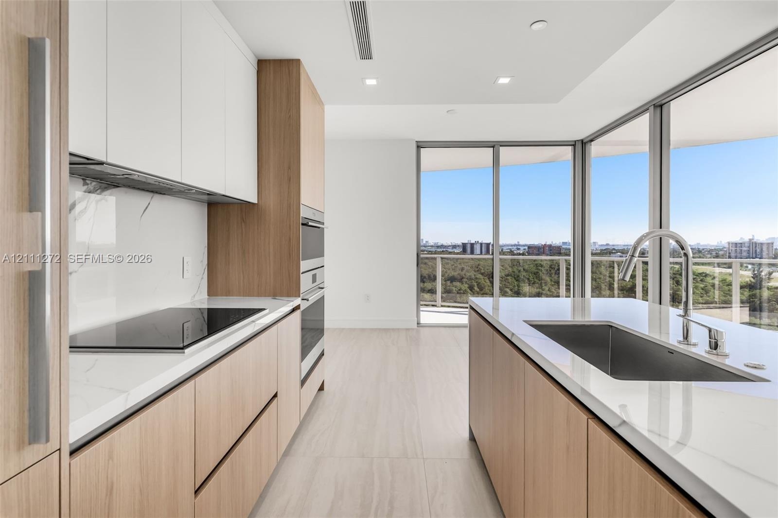 Kitchen featuring wood-finish flat-panel cabinetry, white stone countertops, matching full-height backsplash, built-in stainless steel appliances, and