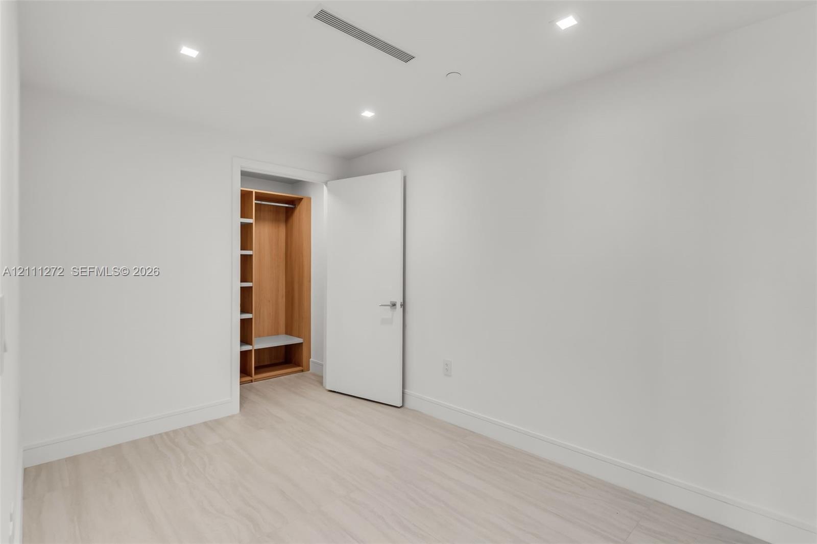 Minimalist room featuring light wood-finish flooring, recessed ceiling lighting, a flush-mount interior door, and a built-in closet with integrated sh
