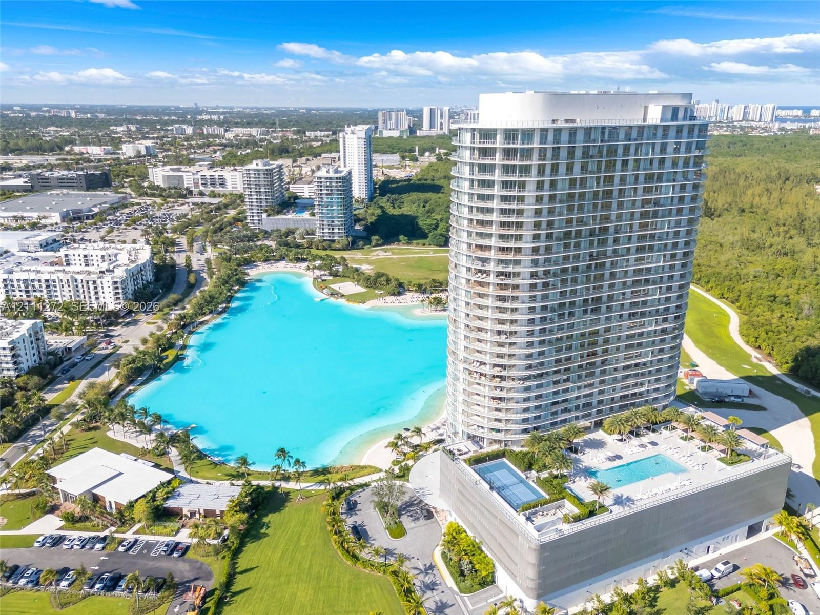 High-rise residential tower featuring a glass-facade exterior, a multi-level podium with an elevated swimming pool, and a large recreational lagoon wi