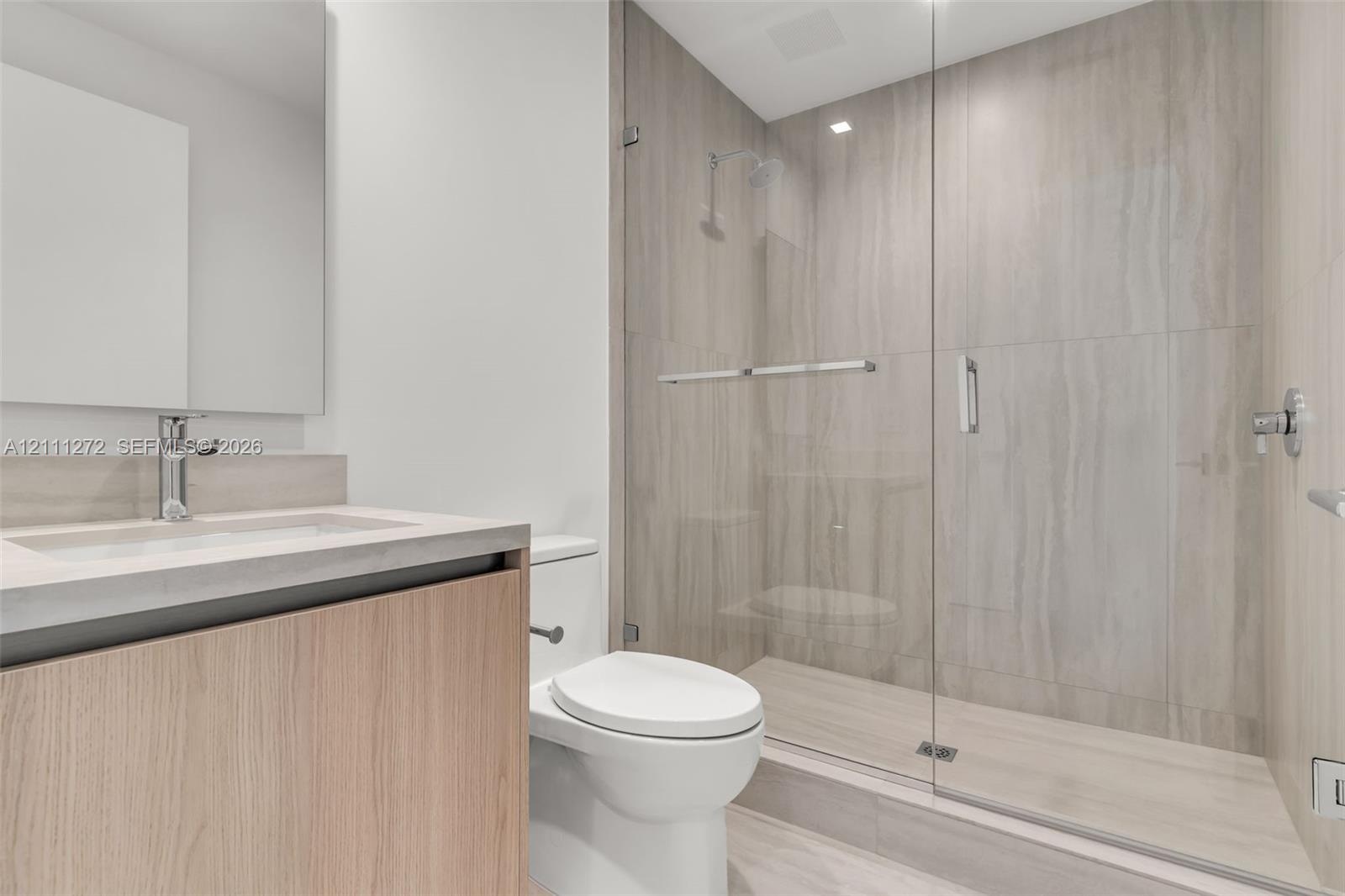 Bathroom featuring a wood-finish vanity with a stone countertop, an integrated sink, polished chrome plumbing fixtures, and a glass-enclosed shower wi