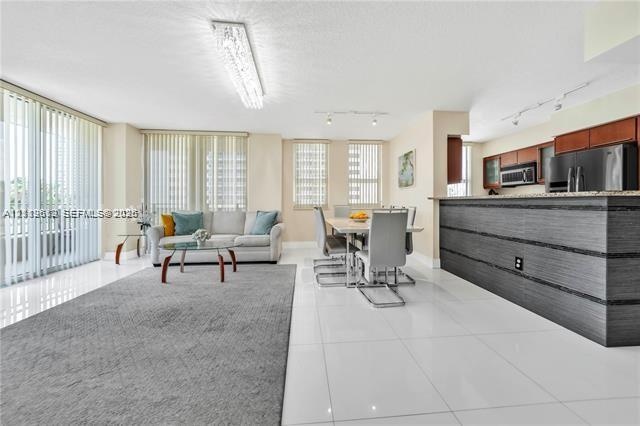 Open-concept interior featuring large-format tile flooring, a kitchen breakfast bar with wood-finish cabinetry, built-in stainless steel appliances, a