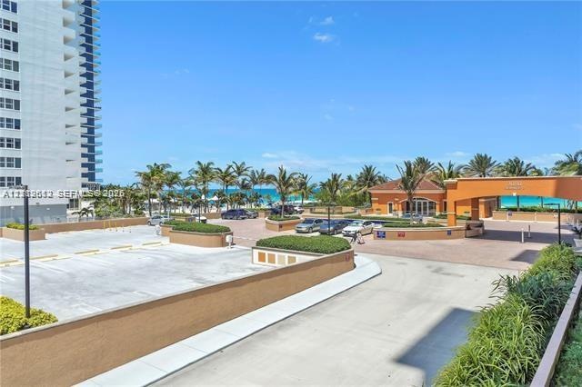 Paved parking area featuring concrete surfaces, stucco perimeter walls, mature palm landscaping, and covered entry portico