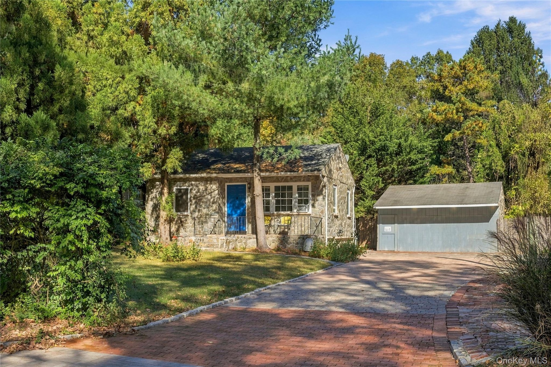 Stone exterior residence featuring a front entry with metal railing, a detached garage, and a brick-paved driveway surrounded by mature trees