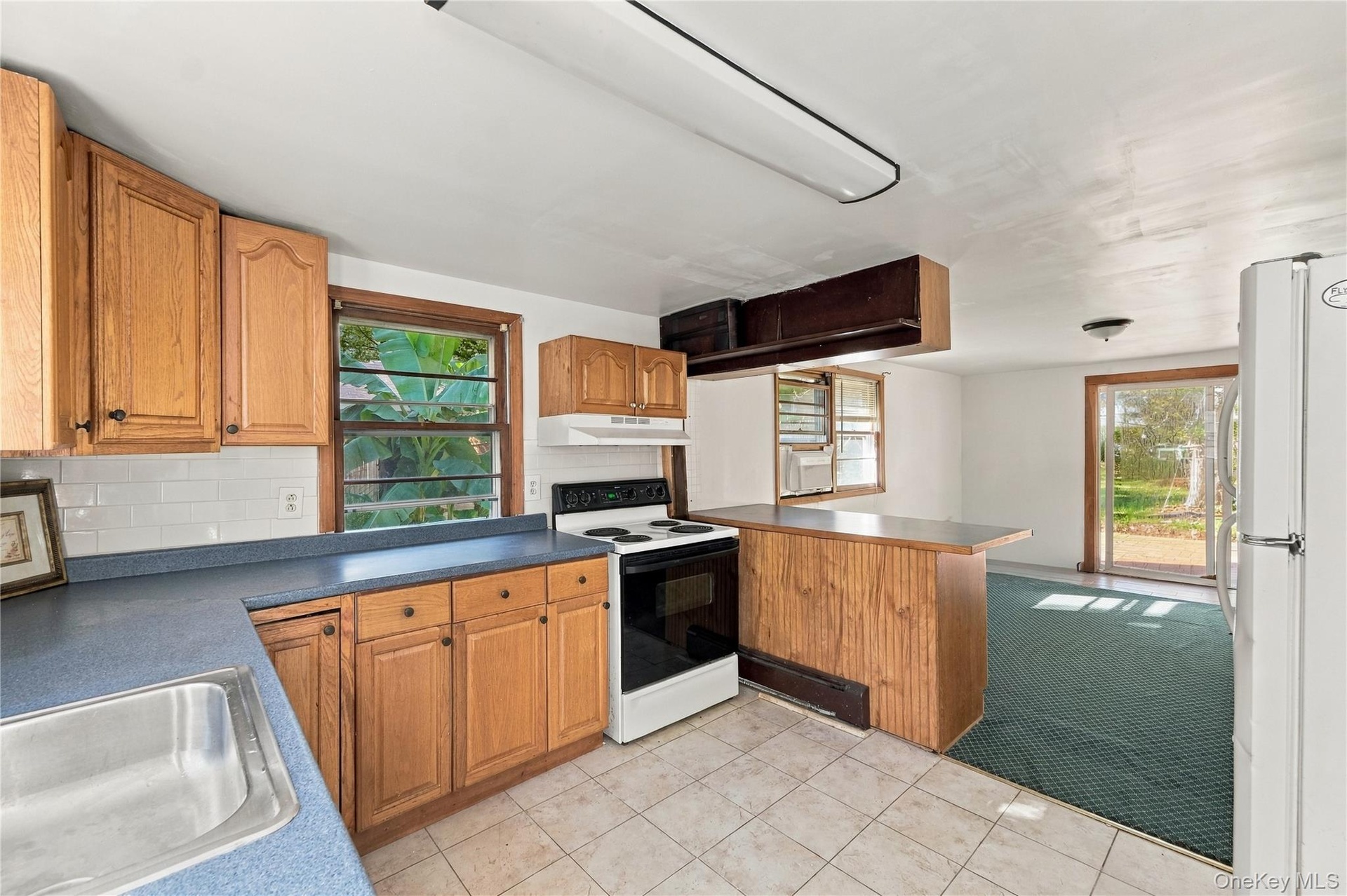 Kitchen featuring light-finish wood cabinetry, solid-surface countertops, tile flooring, built-in breakfast bar, and sliding glass exterior door