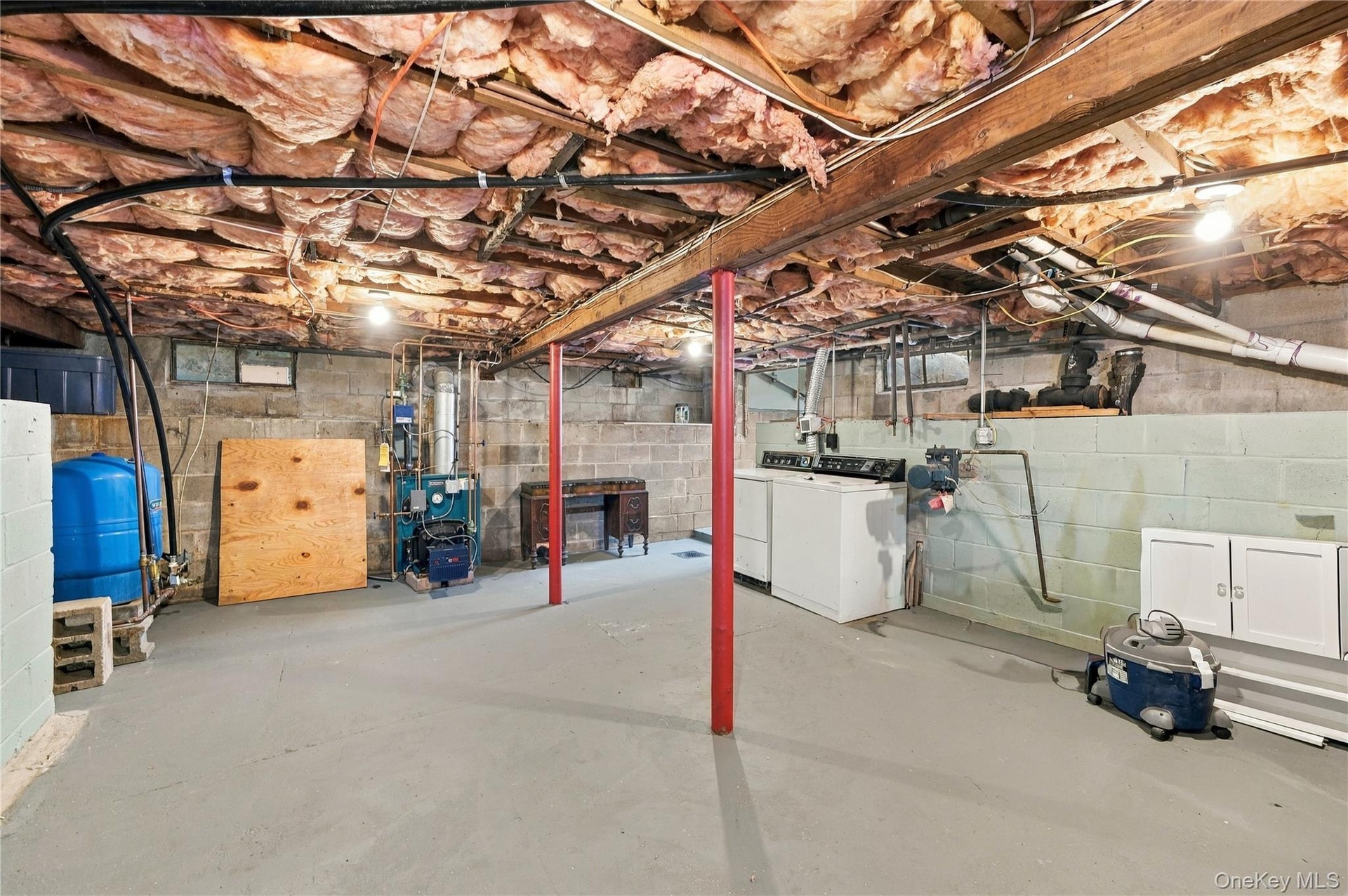 Unfinished basement space featuring exposed joists, painted concrete block walls, concrete floor, support columns, and dedicated laundry hookups