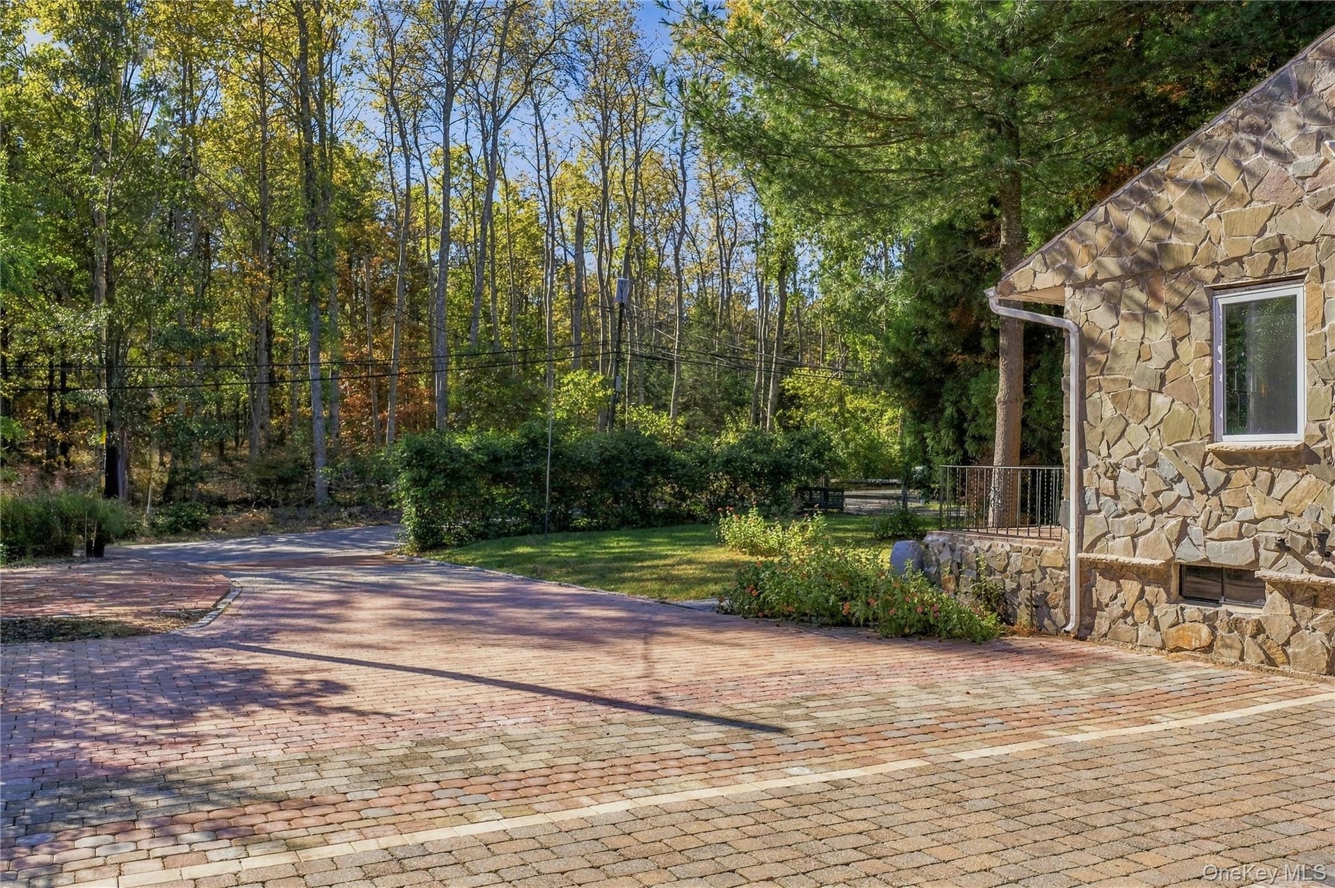 Stone veneer exterior with a multi-toned brick paver driveway and mature perimeter trees