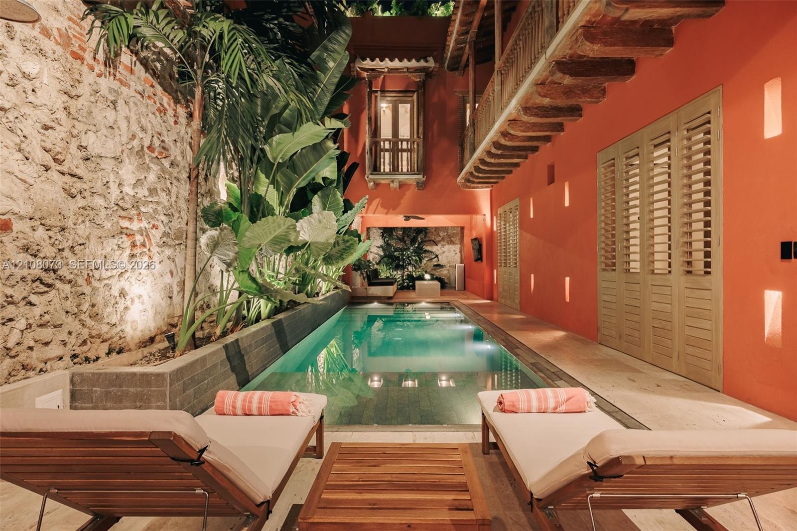 Courtyard featuring a rectangular swimming pool, exposed stone masonry wall, wooden balcony with carved corbels, recessed wall lighting, and louvered 