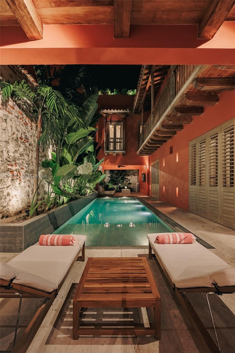 Rectangular pool featuring stone-clad walls, exposed beam ceiling, stone flooring, and built-in louvered shutters