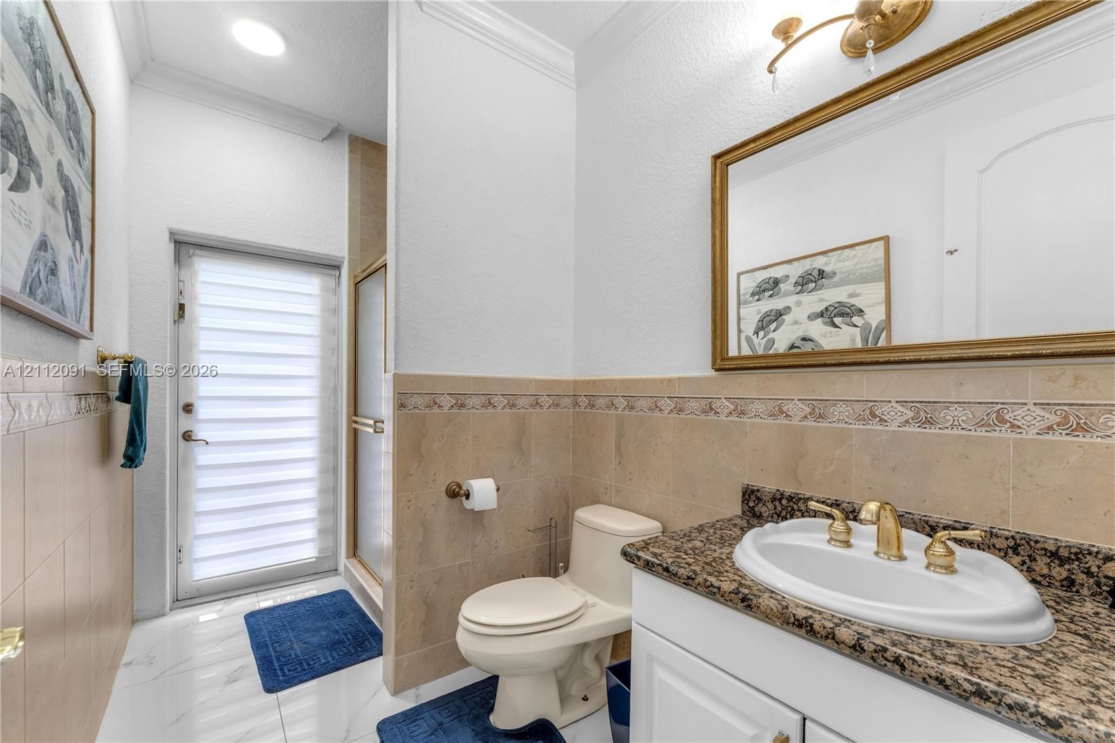 Bathroom featuring stone-finish countertop, undermount sink with gold-tone hardware, decorative tiled wall accent, glass-enclosed shower, and opaque-p