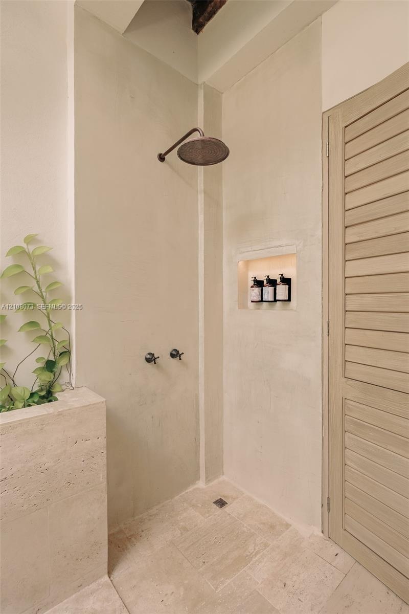 Shower featuring a wall-mounted rain shower head, natural stone wall cladding, built-in recessed wall niche, and stone tile flooring, paired with a lo