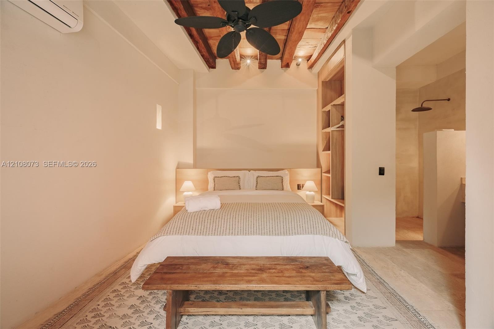 Exposed wood ceiling beams, built-in wooden shelving, wall-mounted air conditioning unit, and matte black ceiling fan