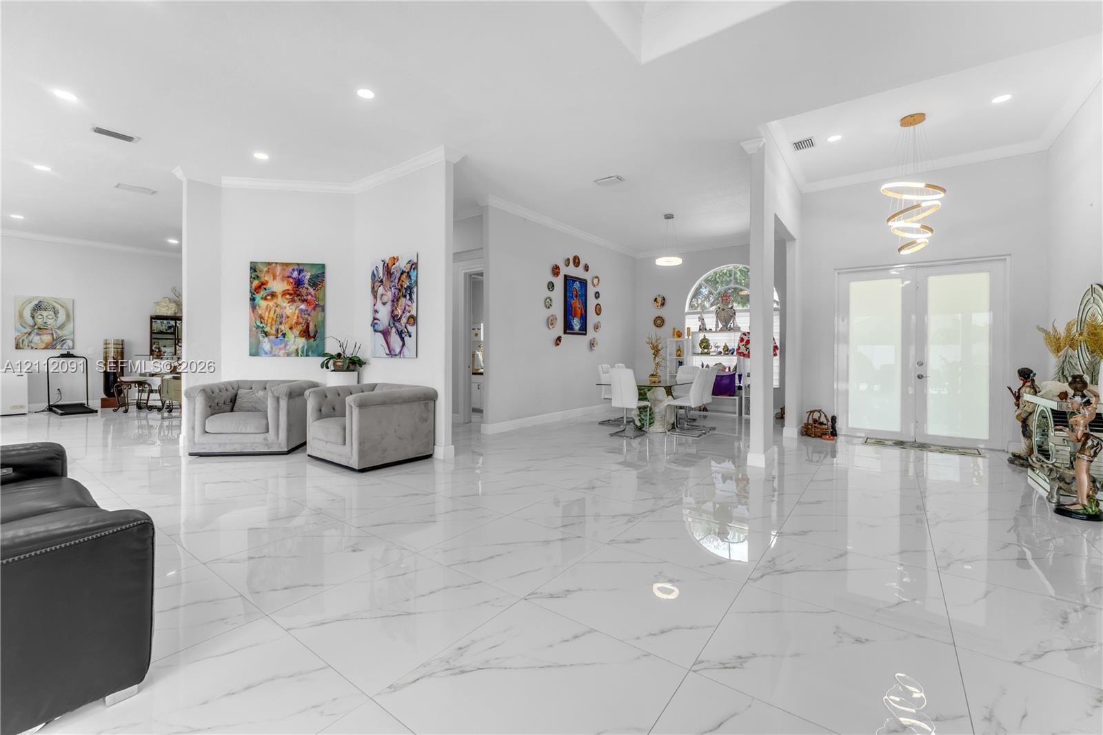Open-concept interior featuring large-format stone-finish tile flooring, recessed ceiling lighting, a modern spiral chandelier, and an arched window