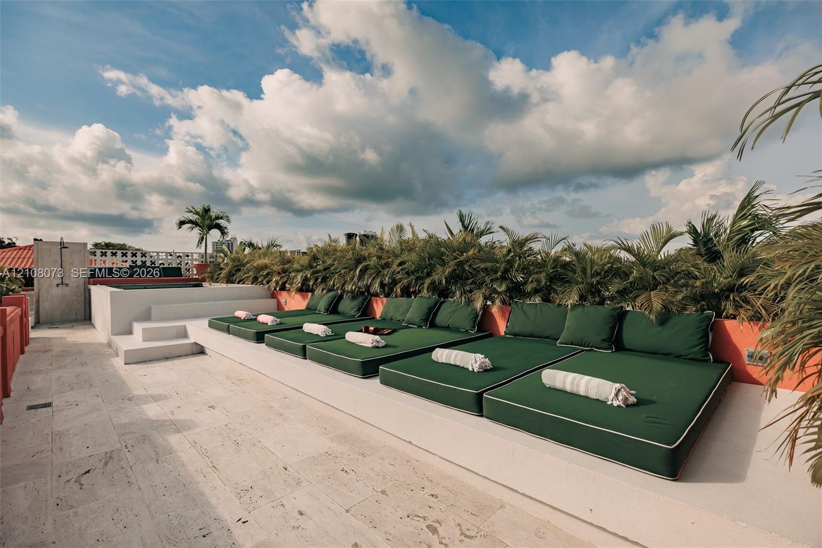 Rooftop terrace featuring natural stone tile flooring, a tiered concrete platform, an outdoor shower, and a built-in privacy wall with decorative bree