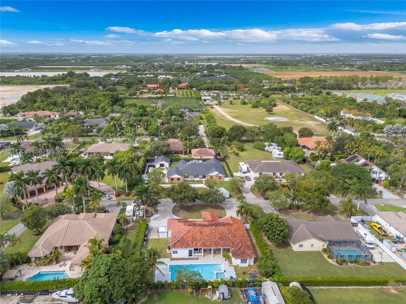 Aerial perspective of a residential property featuring a multi-hipped clay tile roof, a rectangular in-ground swimming pool, a concrete patio area, an