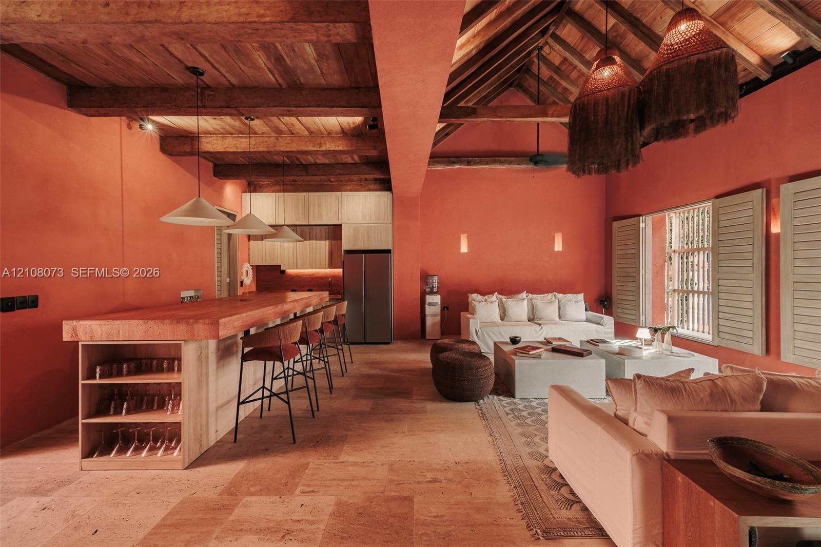 Open-concept living space featuring vaulted ceilings with exposed wood beams, stone tile flooring, a built-in kitchen island with integrated shelving,