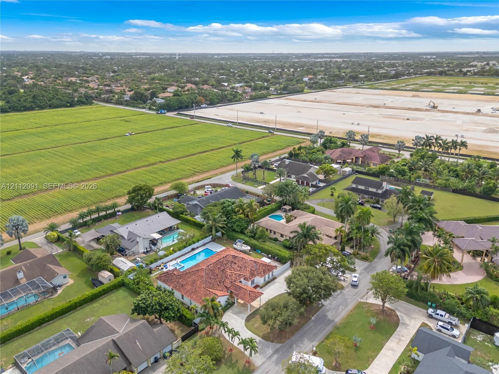 Aerial perspective of a sprawling property featuring a multi-gabled terracotta tile roof, a rectangular swimming pool, an expansive paver driveway, an