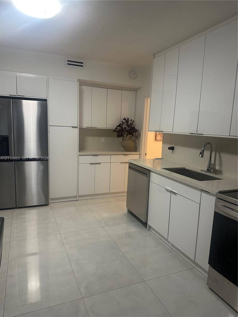 Kitchen featuring flat-panel white cabinetry, stainless steel appliances, light-toned solid surface countertops, and large-format tile flooring
